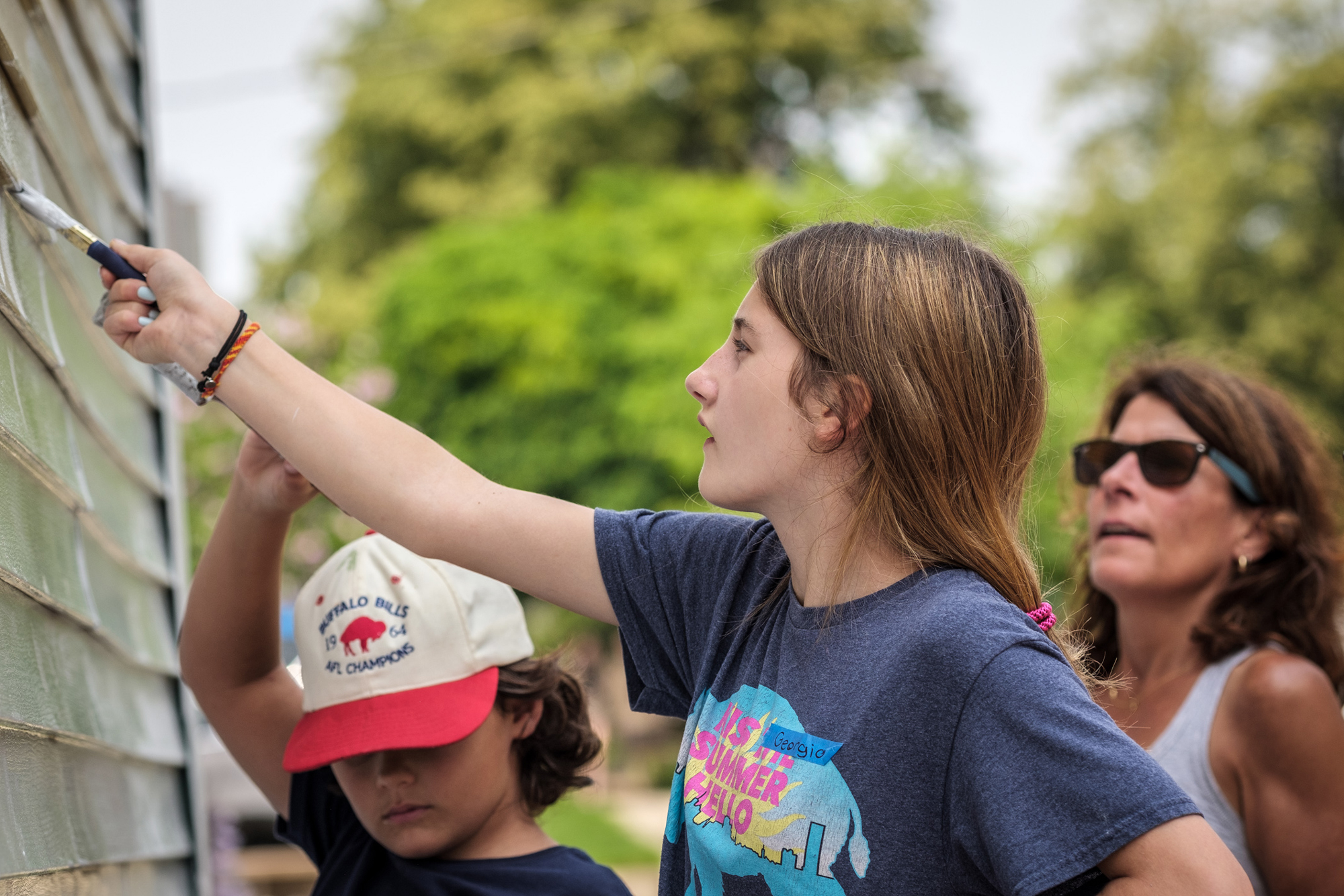 kids painting the side of a house while woman supervises