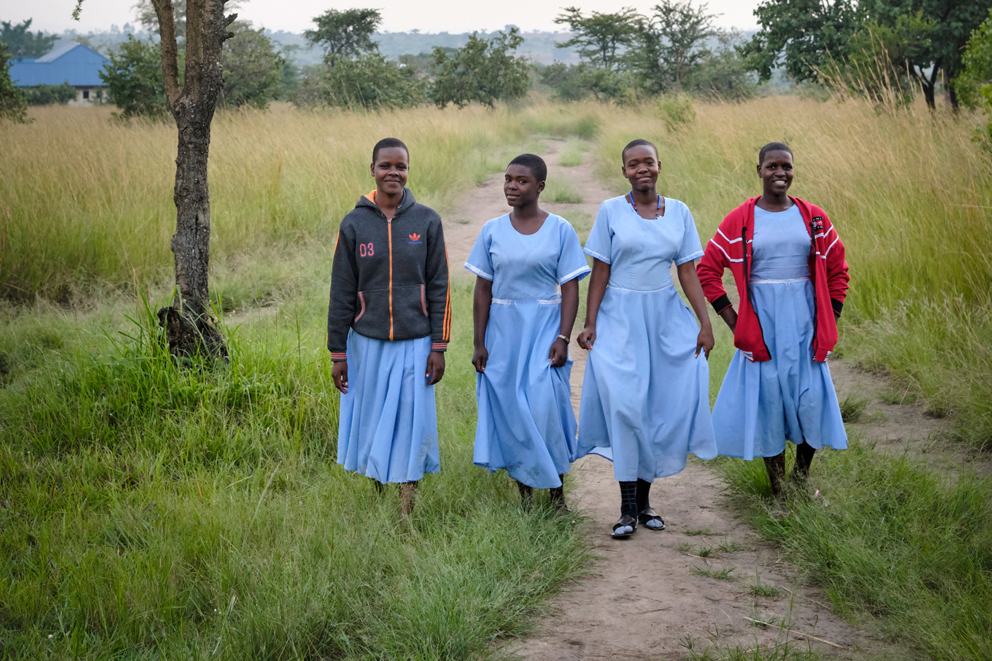 group of four girls walking through a grassy field