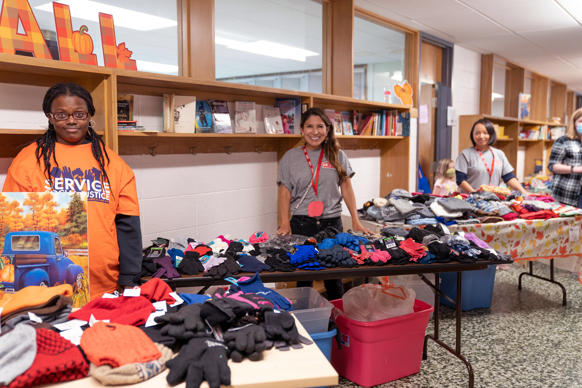 three women standing behind tables filled with winter clothing accessories