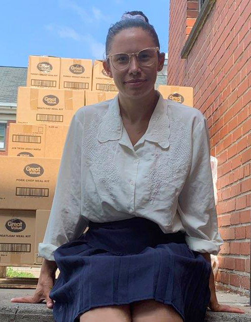 woman sitting on the sidewalk with cardboard boxes of food behind her